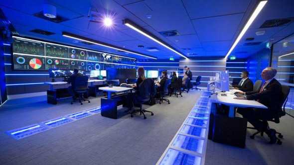 An image of Security Operations Center, with lots of monitors, and very dim light.
